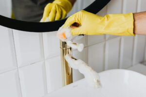 Hand in yellow glove scrubbing a bathroom faucet with soap